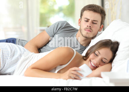 Eifersüchtig Klatsch Mann beobachtete seine Frau Handy auf dem Bett zu Hause Stockfoto