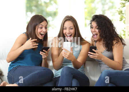 Drei Freunde begeistert beobachtete ein smart Phone sitzen auf einer Couch zu Hause Stockfoto