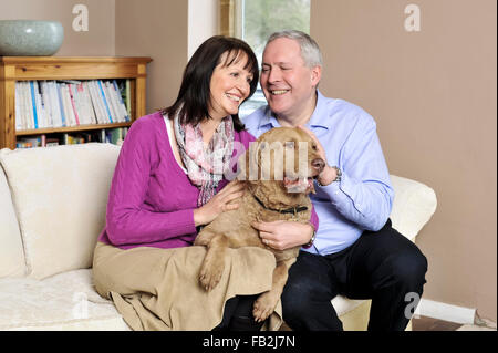 Ein paar mittleren Alters saß auf dem Sofa umarmt ihren Hund Stockfoto