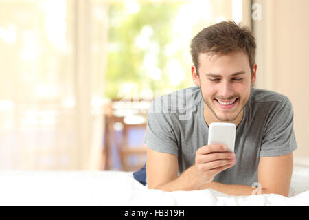 Vorderansicht von einem Kerl mit einem Mobiltelefon im Schlafzimmer zu Hause Stockfoto