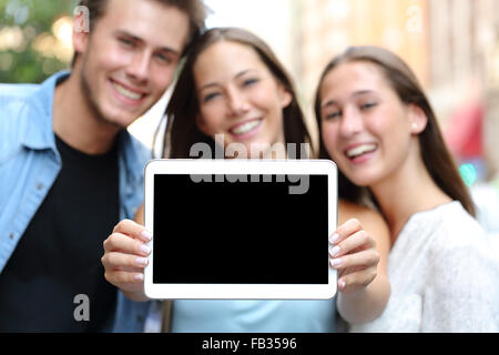 Drei glückliche Freunde zeigen einen leere Tablet-Bildschirm auf der Straße Stockfoto