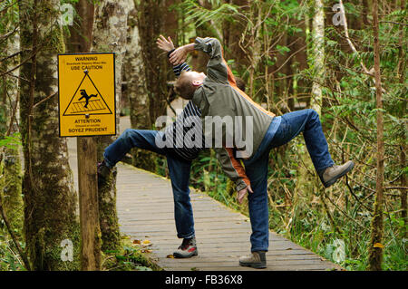 Zwei jungen, die Witze über einen rutschigen, wenn nass Schild an einem Holzsteg im Pacific Rim National Park, BC, Canada Stockfoto