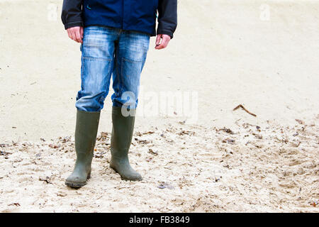 Mann trägt Gummistiefel und im Sand stehen Stockfoto