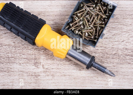 Messingschrauben in Box und Schraubendreher liegen auf hölzernen Tisch-schließen sich Stockfoto