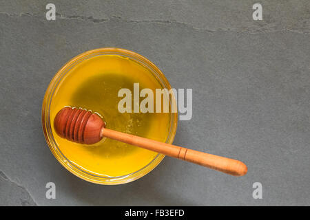 Honig in Glasschale mit hölzernen Honig Dipper, overhead auf Schiefer mit Tageslicht fotografiert Stockfoto
