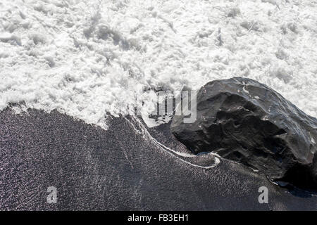 Meerwasser stürzt über einen Basaltfelsen am schwarzen Sandstrand in der Nähe von Vik, Island Stockfoto