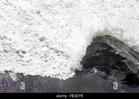 Meerwasser stürzt über einen Basaltfelsen am schwarzen Sandstrand in der Nähe von Vik, Island Stockfoto