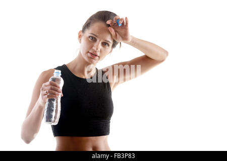 Sportliches Yoga Mädchen auf weißem Hintergrund mit einer Flasche Wasser, Schweiß von der Stirn wischen, nach dem Training Stockfoto