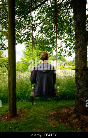 Frau sitzen, sitzen auf der Schaukel hängen hängenden Baum Gartenpark Parkland Blume Blumen Blüte Sommer Stockfoto