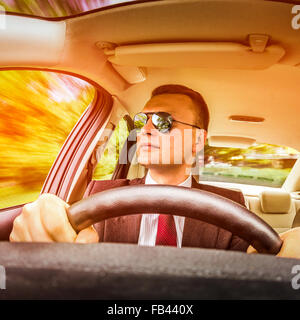 Mann in einem Anzug und Sonnenbrille auf einer Straße im Auto fahren. Stockfoto