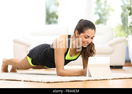 Fitness-Frau auf dem Boden zu Hause trainieren und Ansehen von Fitness-Videos in einer Tablette Stockfoto