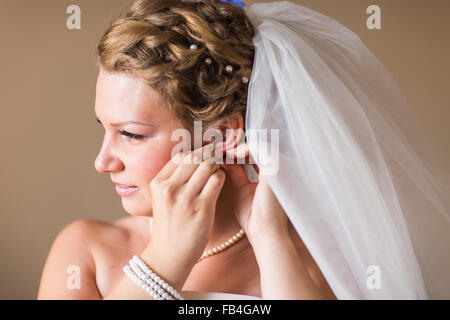 Schöne Braut im weißen Hochzeitskleid setzt auf Ohrring Stockfoto