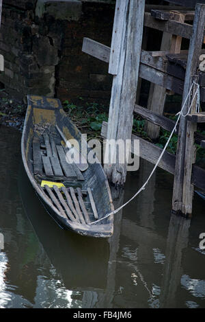 Eine verfallene Holzboot beruht auf das Ende eines zerrissenen Seiles entlang der Pfähle eines Pier am Inle-See in Myanmar. Stockfoto