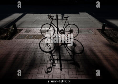 Ein Fahrrad & es werfen Schatten auf einem Ziegel Bürgersteig entlang State Street in Santa Barbara, Kalifornien erstellt ein symmetrisches Muster. Stockfoto