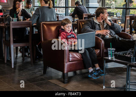 Technisch versierte junge 10-12 Jahre alt, sitzt in einem Café mit einem großen Laptop auf seinem Schoß, wie konzentriert er sich auf sie. Stockfoto