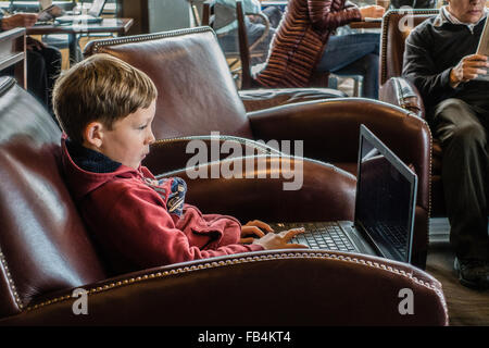 Technisch versierte junge 10-12 Jahre alt, sitzt in einem Café mit einem großen Laptop auf seinem Schoß, wie konzentriert er sich auf sie. Stockfoto