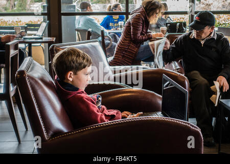 Technisch versierte junge 10-12 Jahre alt, sitzt in einem Café mit einem großen Laptop auf seinem Schoß, wie konzentriert er sich auf sie. Stockfoto