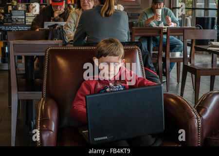 Technisch versierte junge 10-12 Jahre alt, sitzt in einem Café mit einem großen Laptop auf seinem Schoß, wie konzentriert er sich auf sie. Stockfoto