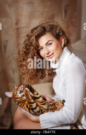 Mädchen und Leopard Katze nach Hause. Wohnkomfort. Katze spielt mit lockigem Haar Mädchen. Stockfoto