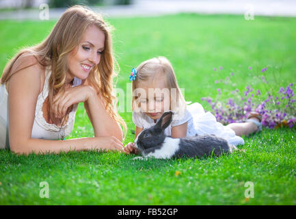 Junge Frau und ihre Tochter mit einem Haustier Kaninchen in einem Park spielen Stockfoto