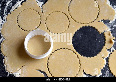 Rollte Teig mit einem Cookie Cutter und mehrere Kreise ausschneiden, auf einer dunklen Arbeitsplatte Stockfoto