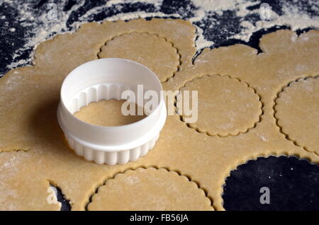 Rollte Teig mit einem Cookie Cutter und mehrere Kreise ausschneiden, auf einer dunklen Arbeitsplatte Stockfoto