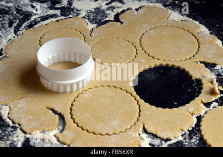 Rollte Teig mit einem Cookie Cutter und mehrere Kreise ausschneiden, auf einer dunklen Arbeitsplatte Stockfoto