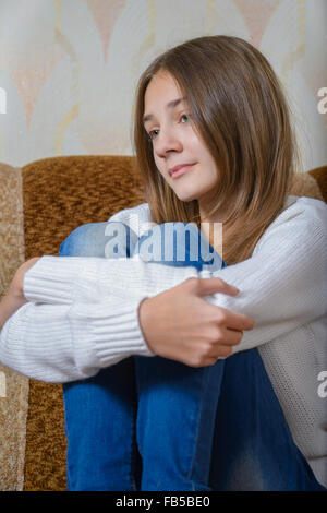 Ein Mädchen in einem weißen Pullover und Jeans sitzt auf der Couch und Träume Stockfoto