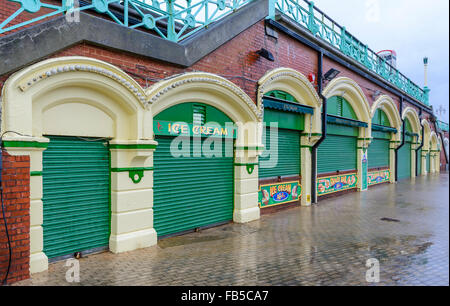 Geschlossene Geschäfte mit Rollläden unten am Meer an einem regnerischen Tag im Winter in Brighton, East Sussex, England, UK. Stockfoto