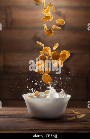 Fallende Cornflakes mit Milch Spritzen auf hölzernen Hintergrund Stockfoto