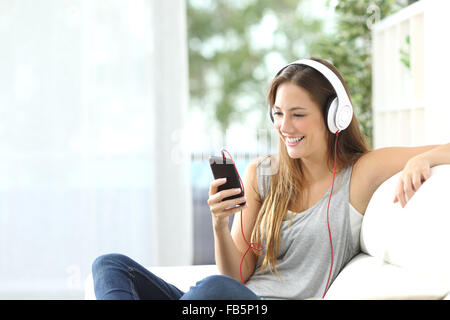 Glückliches Mädchen anhören von Musik vom Handy auf einer Couch zu Hause sitzend Stockfoto