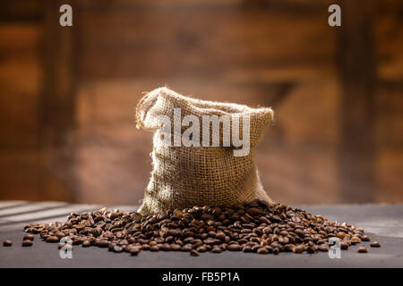 Kaffeebohnen mit Dampf in Tasche am schwarzen Tisch aus Holz Hintergrund Stockfoto