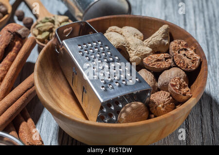 Ingwer mit Muskatnuss und Reibe in Schüssel auf hölzernen Hintergrund und verschiedenen Gewürzen Stockfoto