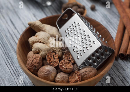 Ingwer mit Muskatnuss und Reibe in Schüssel auf hölzernen Hintergrund und verschiedenen Gewürzen Stockfoto