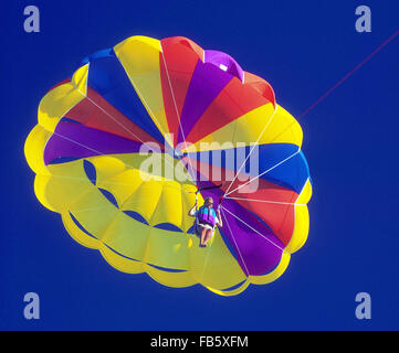 Weiblichen Urlauber im Urlaub auf den Florida Keys nimmt eine mehrfarbige Parasailing Fahrt hoch am blauen Himmel in Islamorada, Florida, USA. Stockfoto