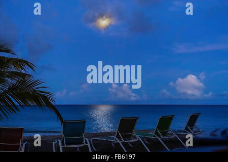 ein Vollmond kämpft sich durch die Wolken über dem karibischen Meer. Nacht-Zeit-Strand-Szene. Stockfoto