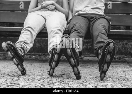 Menschen Freunde im Trainingsanzug mit Rollschuhen. Frau und Mann auf Bank im Freien entspannen. Stockfoto