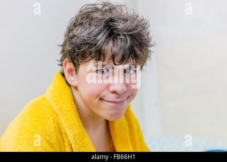 junge zerzaust und leicht gebeugt in gelben Bademantel macht Gesichter Stockfoto