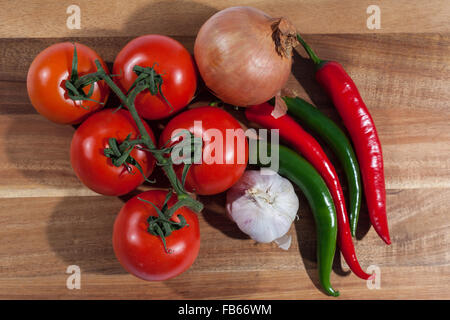 Fünf Strauchtomaten, Knoblauchzwiebel, eine Zwiebel und vier Chilischoten auf ein Schneidebrett von oben Stockfoto