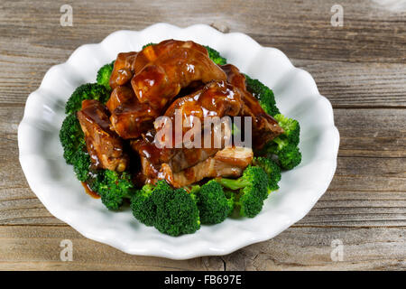 Nahaufnahme gegrilltes Rindfleisch Rippen, in extra Soße und Brokkoli in weißer Teller auf rustikalen Holz Rahmen. Stockfoto