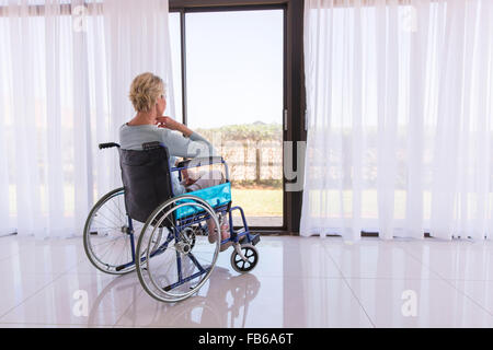 nachdenklich behinderte Frau im Rollstuhl durch Türglas Stockfoto