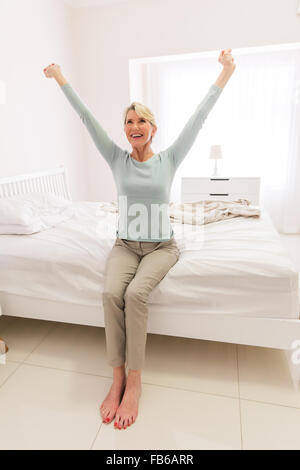 lächelnd Mitte im Alter Frau sitzt auf dem Bett und stretching Stockfoto