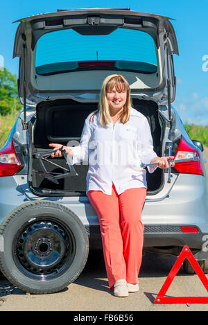 50 Jahre alt, lächelnde Frau in der Nähe von das Auto mit einem Reifenschaden Stockfoto