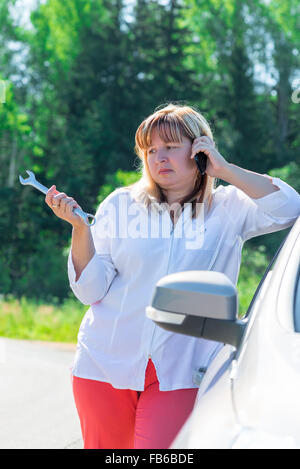 Porträt einer Frau mit einem Schraubenschlüssel in der Nähe von dem kaputten Auto Stockfoto