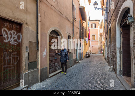 Kaukasischen Mann mittleren Alters mit grauen Haaren, gekleidet in schwarze Daunenjacke zu Fuß den alten Straßen und Gassen von Rom, Italien Stockfoto