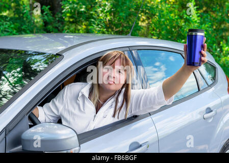 Reife Frau mit einem Getränk sieht aus dem Autofenster während der Fahrt Stockfoto