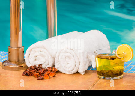 Zwei gerollte Handtücher und eine Tasse Tee am Pool Stockfoto