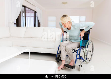 behinderte Frau, die versucht, Aufstehen vom Rollstuhl im Wohnzimmer Stockfoto