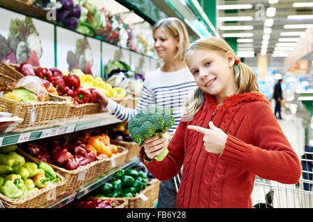 Glückliches Mädchen zeigt Brokkoli im Supermarkt Stockfoto