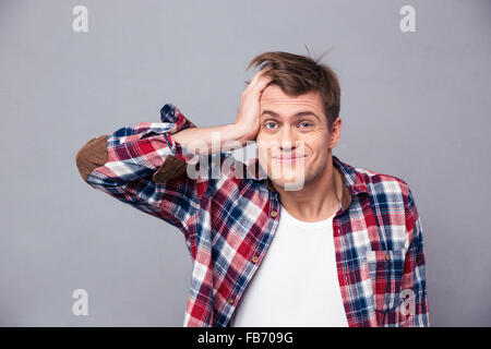 Nahaufnahme von peinlich junger Mann im karierten Hemd Kopf kratzen und verwirrt mit Blick auf grauem Hintergrund Stockfoto